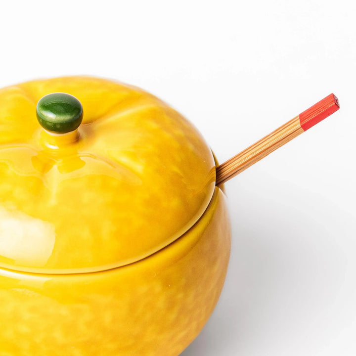 A small ceramic container shaped like a yuzu fruit with a lid and a spoon, bright yellow color.